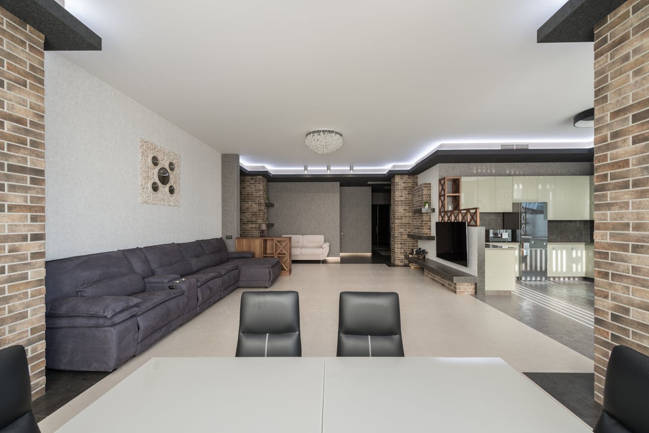 Table with chairs placed in living room with comfortable couch and TV near kitchen zone with cupboards in stylish apartment
