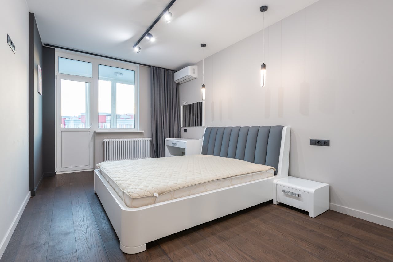 Spacious minimalist bedroom featuring modern design elements with white walls and parquet flooring.